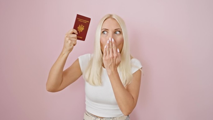 震惊的年轻金发女子用手捂住嘴，在粉红色的孤立背景上显示出恐惧的表情，法国护照暴露了她的巨大错误。
