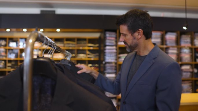 一位白人顾客在一家男装店寻找零售陈列的西装