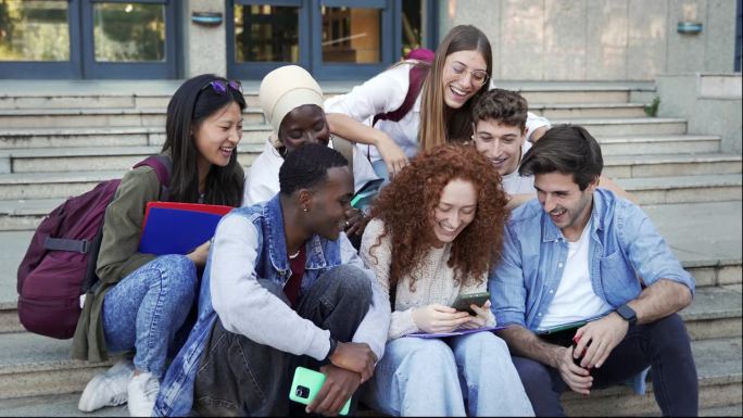 微笑的大学生朋友一起使用移动设备，在社交网络上看搞笑视频