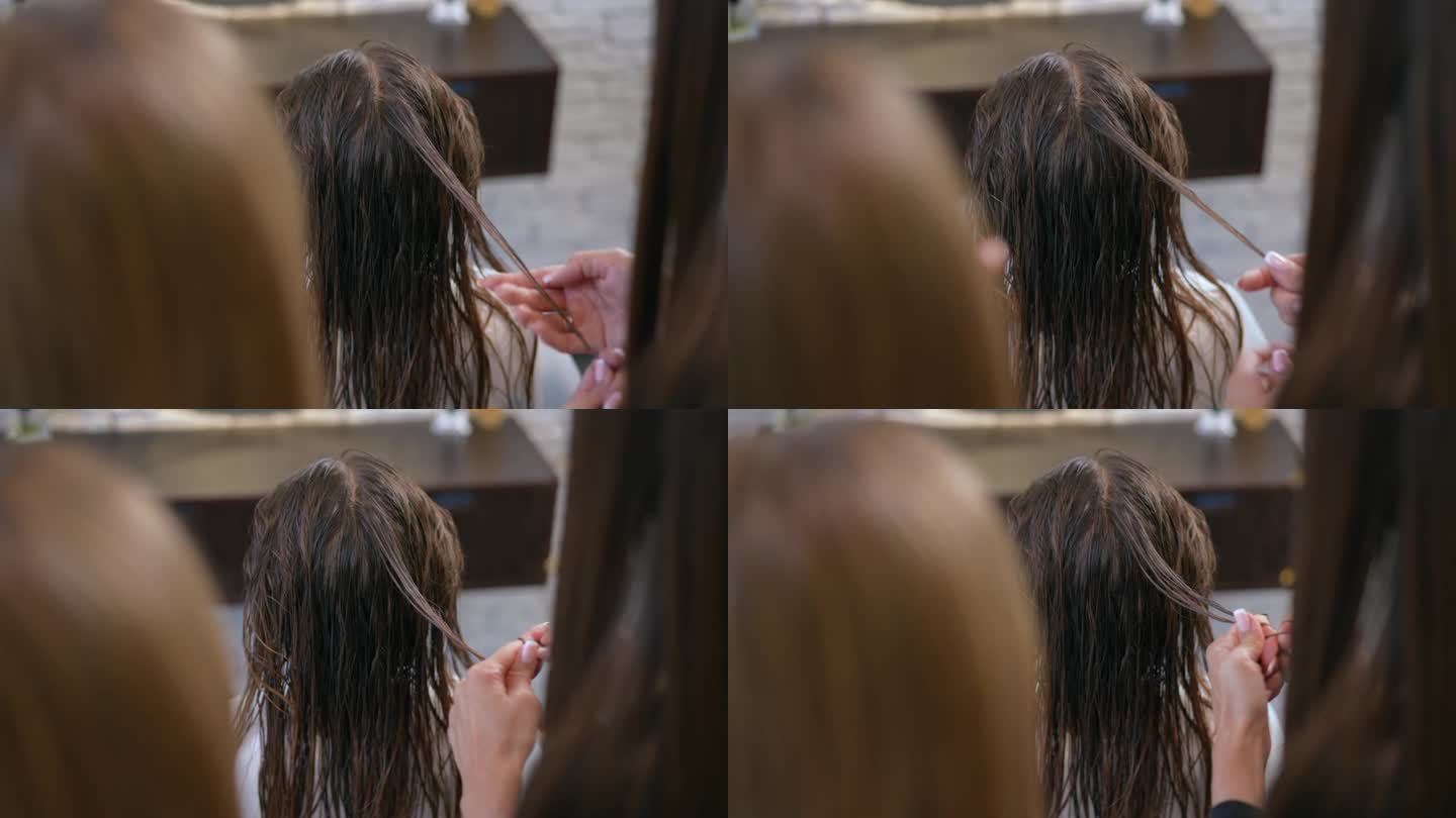 后面的观点。沙龙里，一个女孩湿着头发坐在椅子上。女理发师检查一个女孩的一缕湿发是否有力量。