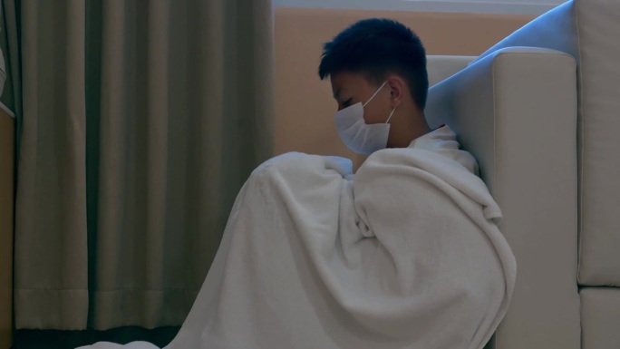 戴着面具的亚洲男孩的脸生病了坐在黑暗中，思考着冲突，家庭关系。悲伤的脸，不开心的孩子低着头坐着，情绪