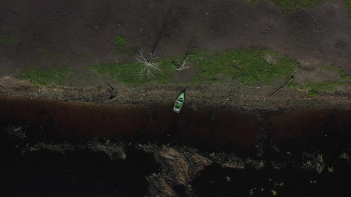 从天空:无人机镜头揭示了一艘渔船停泊在岸边，设置在蓝色和绿色的和谐背景下，由散落的倒下的树林增强。