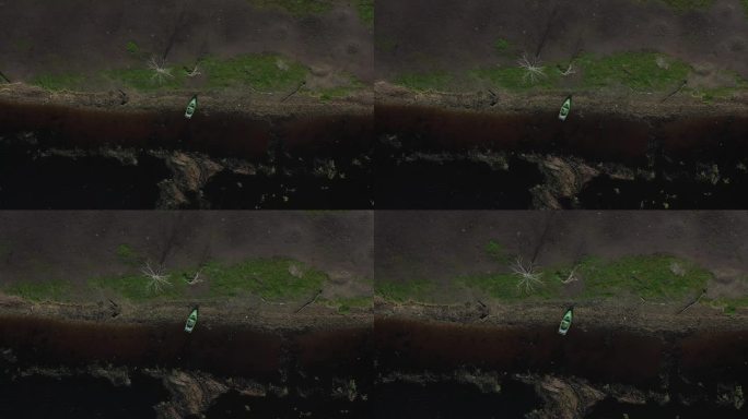从天空:无人机镜头揭示了一艘渔船停泊在岸边，设置在蓝色和绿色的和谐背景下，由散落的倒下的树林增强。