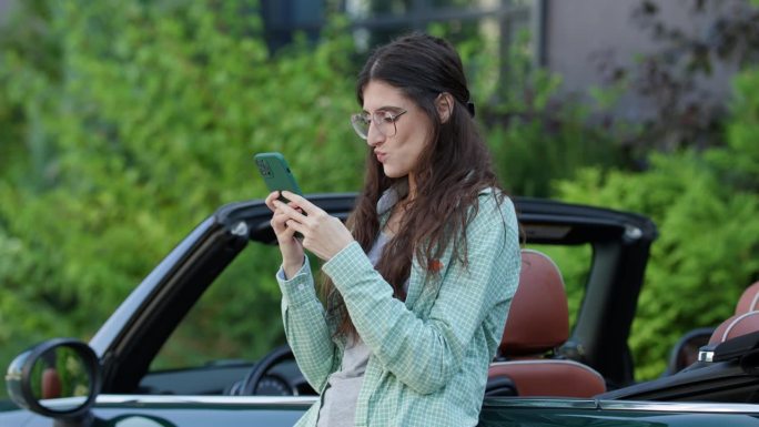 站在敞篷车里用手机发短信的女人。司机在车旁浏览智能手机。