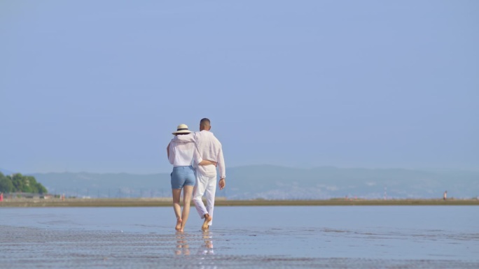 一对情侣在阳光明媚的海滩上拥抱着散步