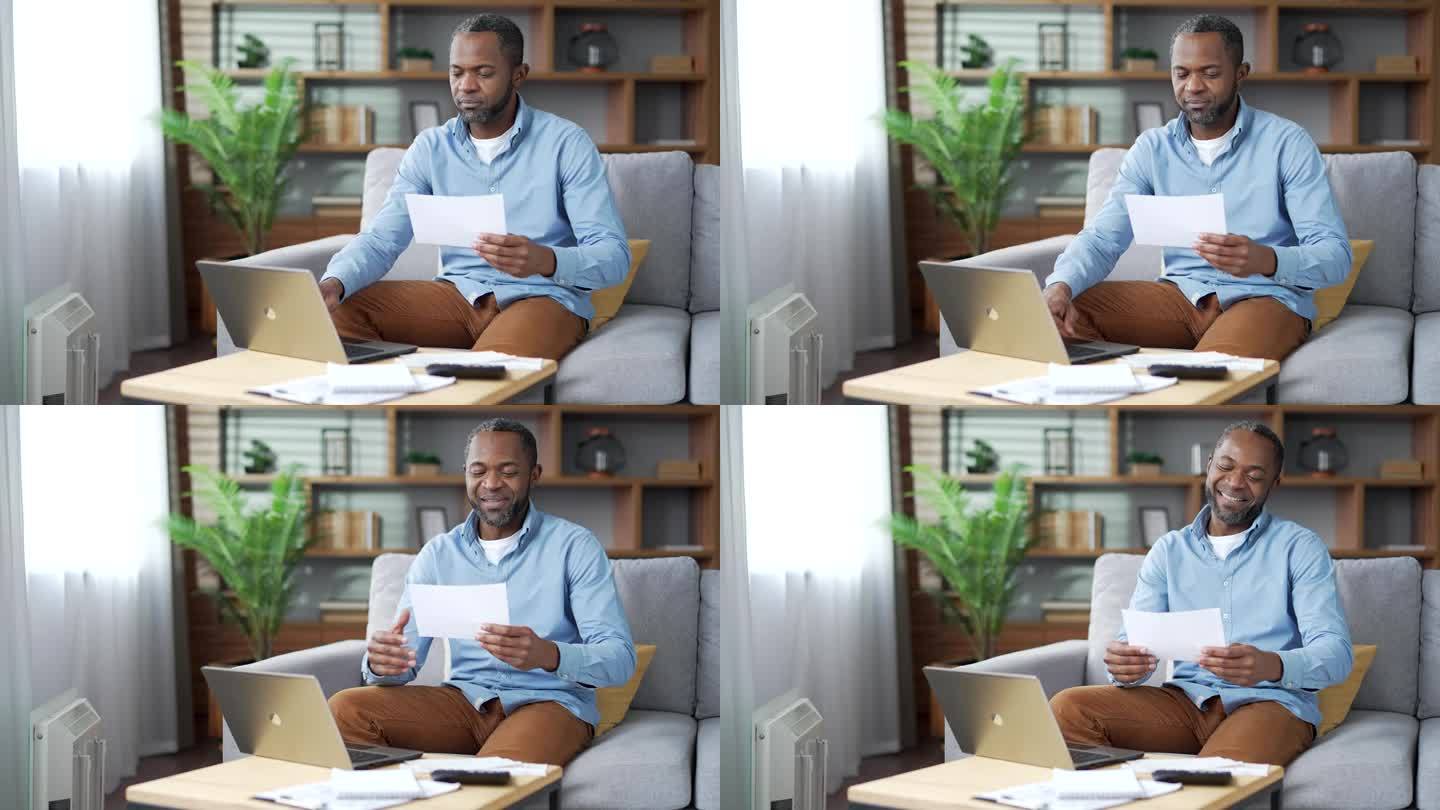 一个成熟的非裔美国人坐在家里的房间里用笔记本电脑申请消费账单