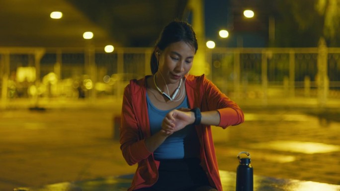 年轻的亚洲女运动员跑步者在城市夜间户外运动前，在智能手表上检查进度并查看智能手表心率监测器。健康的锻