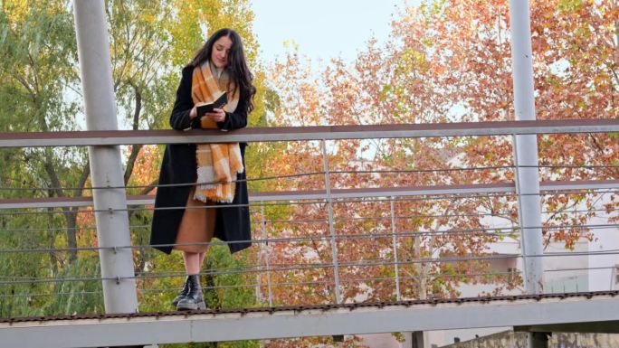 秋日黄昏的公园里，一位身穿大衣、围着围巾的妇女在笔记本上写字