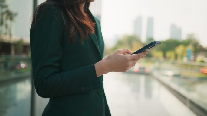 近距离观察年轻的亚洲女商人使用手机，通过在线消息与人聊天，在休息时间站在户外办公室，商务人士用智能技