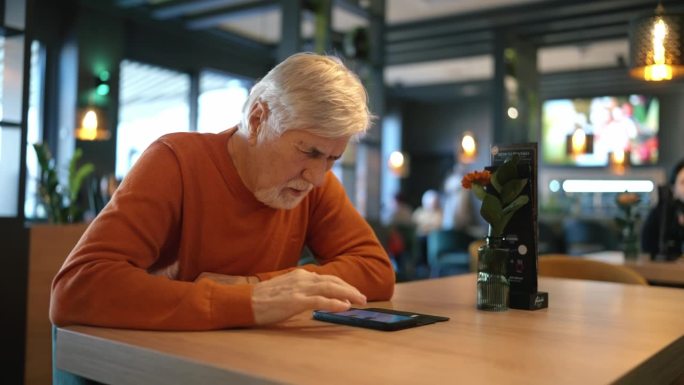 穿着便服的成年老人在咖啡馆的餐桌上玩智能手机