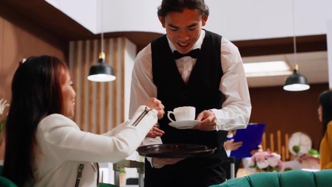 年轻服务员在休息区为亚洲客人端上咖啡