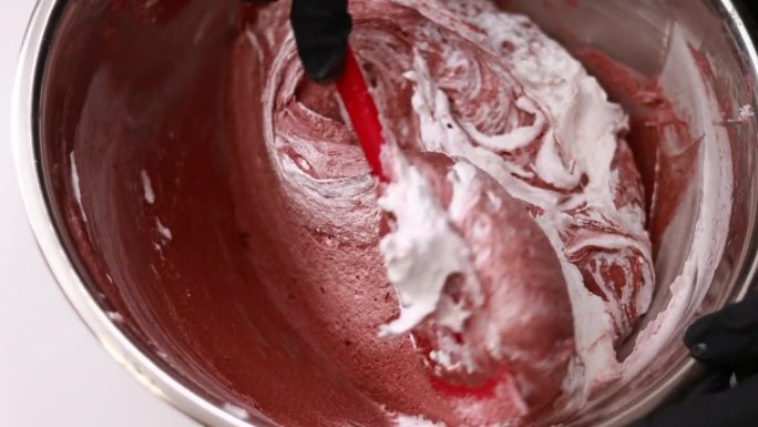 糕点师将硅胶刮刀和制作法式甜点马卡龙的棕色面团混合在一个不锈钢碗里，这是制作蛋糕的过程。糖果店或糕点