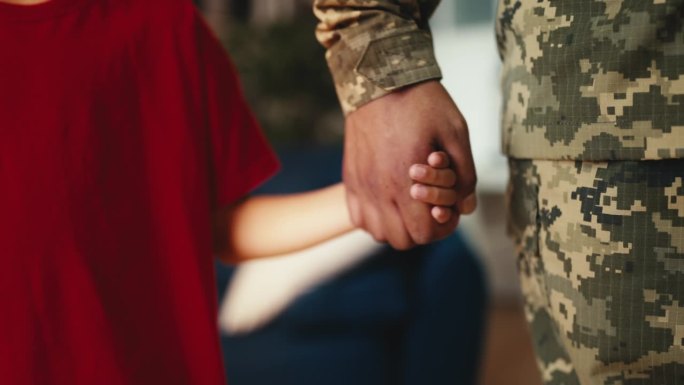 小男孩牵着士兵父亲的手，父母要去服兵役了