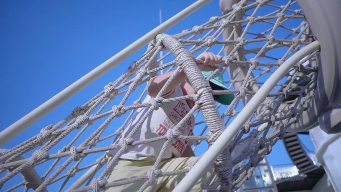 蓝天下的操场上，一个小男孩在绳网上攀爬。