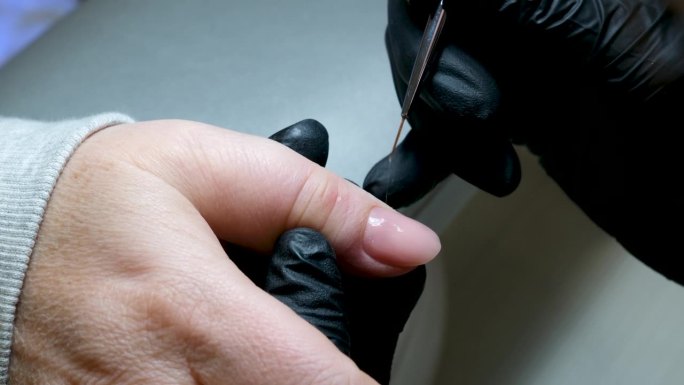 美甲师将指甲的角质层加工成一种特殊的设备，使用指甲刀清洁指甲。宏。特写卸妆啫喱，美甲机，女师傅。美甲