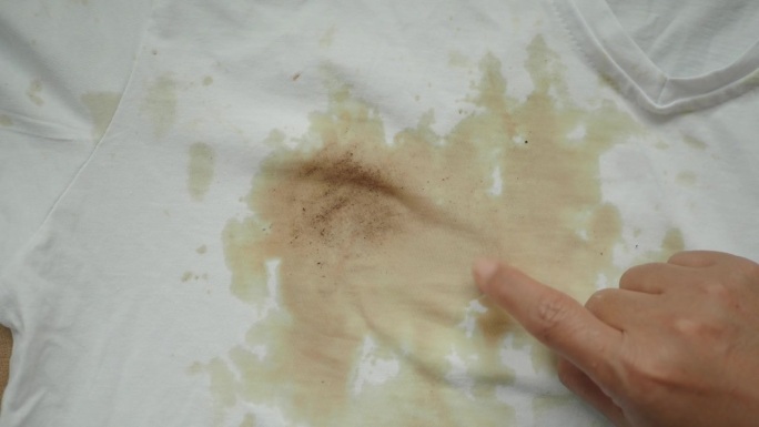 妇女拿着白色的脏衬衫，露出制造的污迹