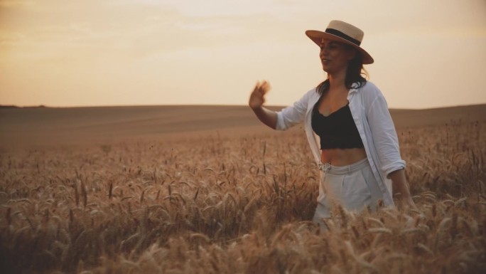 夕阳下快乐的女人漫步在金色的麦田里