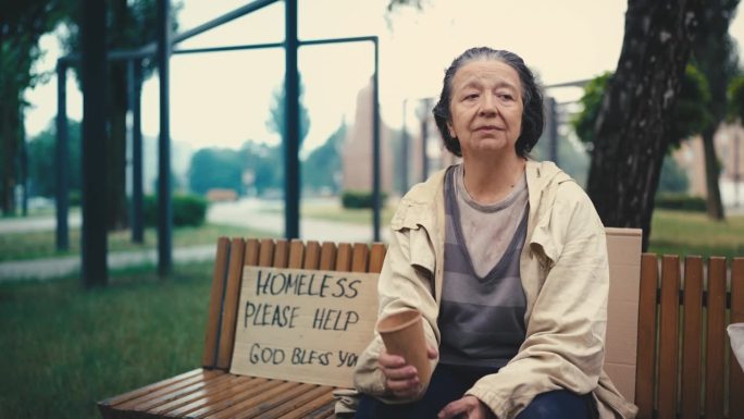 不幸的无家可归的女人拿着纸杯乞讨，冷漠的人们无视她
