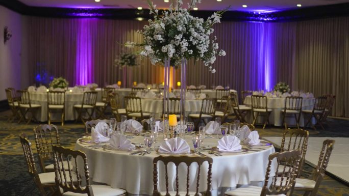 为婚礼装饰的圆桌，高大的中心饰有凤尾花、白玫瑰和绿叶。
