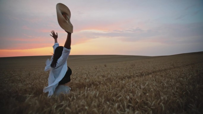 日落时分，拿着帽子在麦田里奔跑的快乐女子