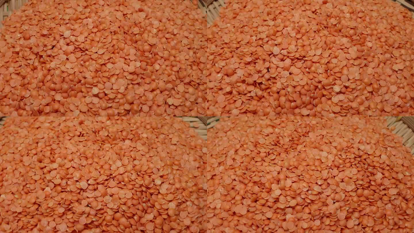 红色的小扁豆在质朴的圆形编织竹盘上旋转，落在绿色的背景上移动