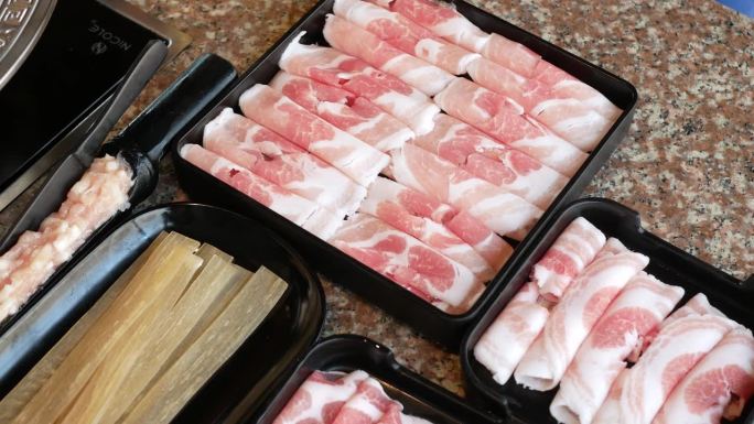 托盘里的猪肉牛肉片、腌肉和中式干面摆上餐桌，准备烹制中式四川风味火锅，合家欢用餐。