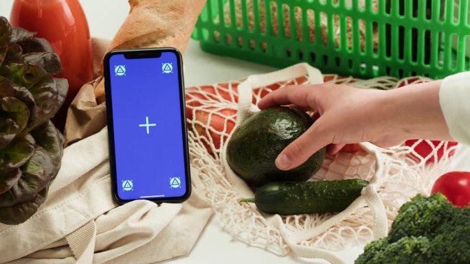 食品购物配送，网上商店应用，蓝色度键屏智能手机和新鲜蔬菜。在超市买吃的。