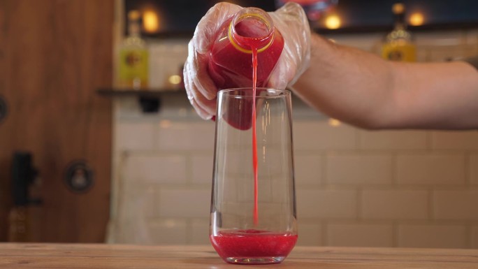 酒保把浓稠的浆果汁倒进杯子里，做成浆果柠檬水。