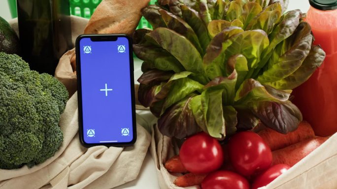 食品购物配送，网上商店应用，蓝色度键屏智能手机和新鲜蔬菜。在超市买吃的。