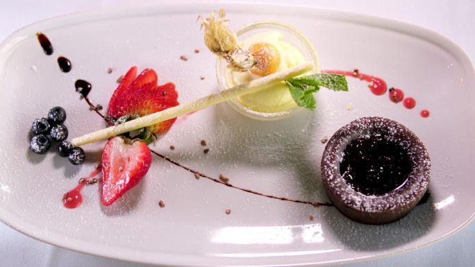 白色盘子里的巧克力软糖配上黑巧克力冰淇淋，草莓糖浆，在昂贵的餐厅里是一道美丽的甜点