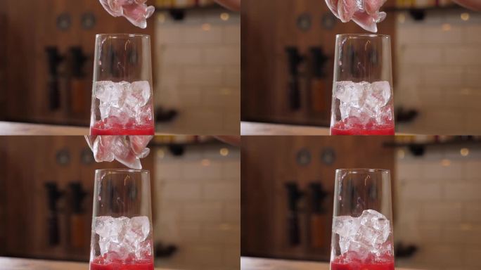 一个戴着手套的调酒师把冰块放进装有浆果汁的杯子里的特写镜头。