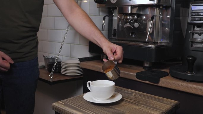咖啡师将浓缩咖啡倒入杯中，加入搅打过的牛奶，制成香味扑鼻的咖啡