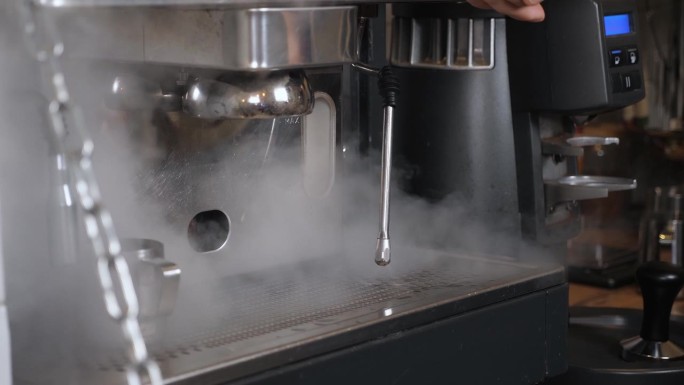 一名男子打开咖啡机上的蒸发器，蒸汽被倒入一个滴漏盘。