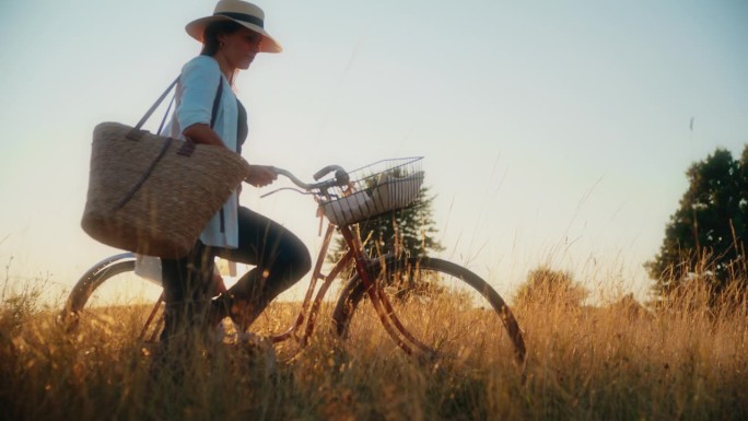 SLO MO女子拿着自行车和肩包享受阳光明媚的草地