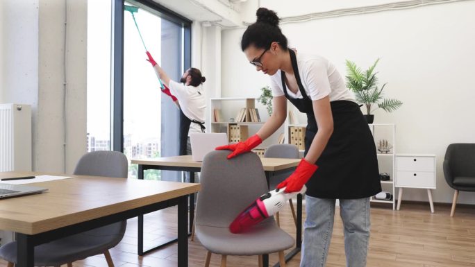 多民族女清洁工带便携式吸尘器的吸尘椅。