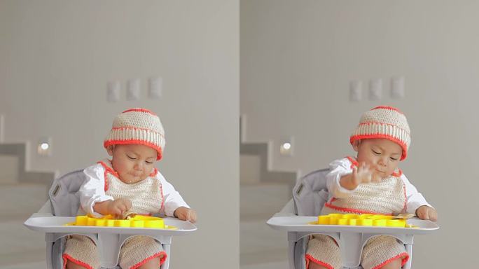 一个婴儿坐在椅子上用手从硅胶盘子里拿东西吃。婴儿主导的断奶概念