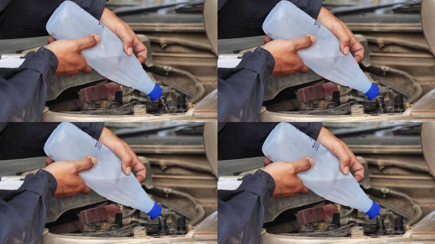 汽车修理工正在为汽车蓄电池机械维修倒去离子纯化蒸馏水。近距离手男子拿去离子蒸馏水瓶在车库汽车移动汽车