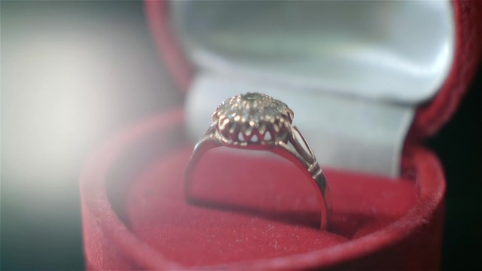 一枚漂亮的金戒指，镶着许多宝石，红色的盒子在阳光下闪闪发光