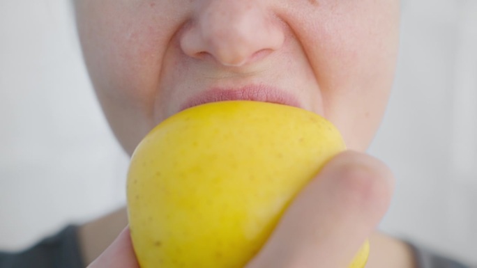 一个吃素的女人咬下一个熟透的黄苹果，这是特写。素食点心。
