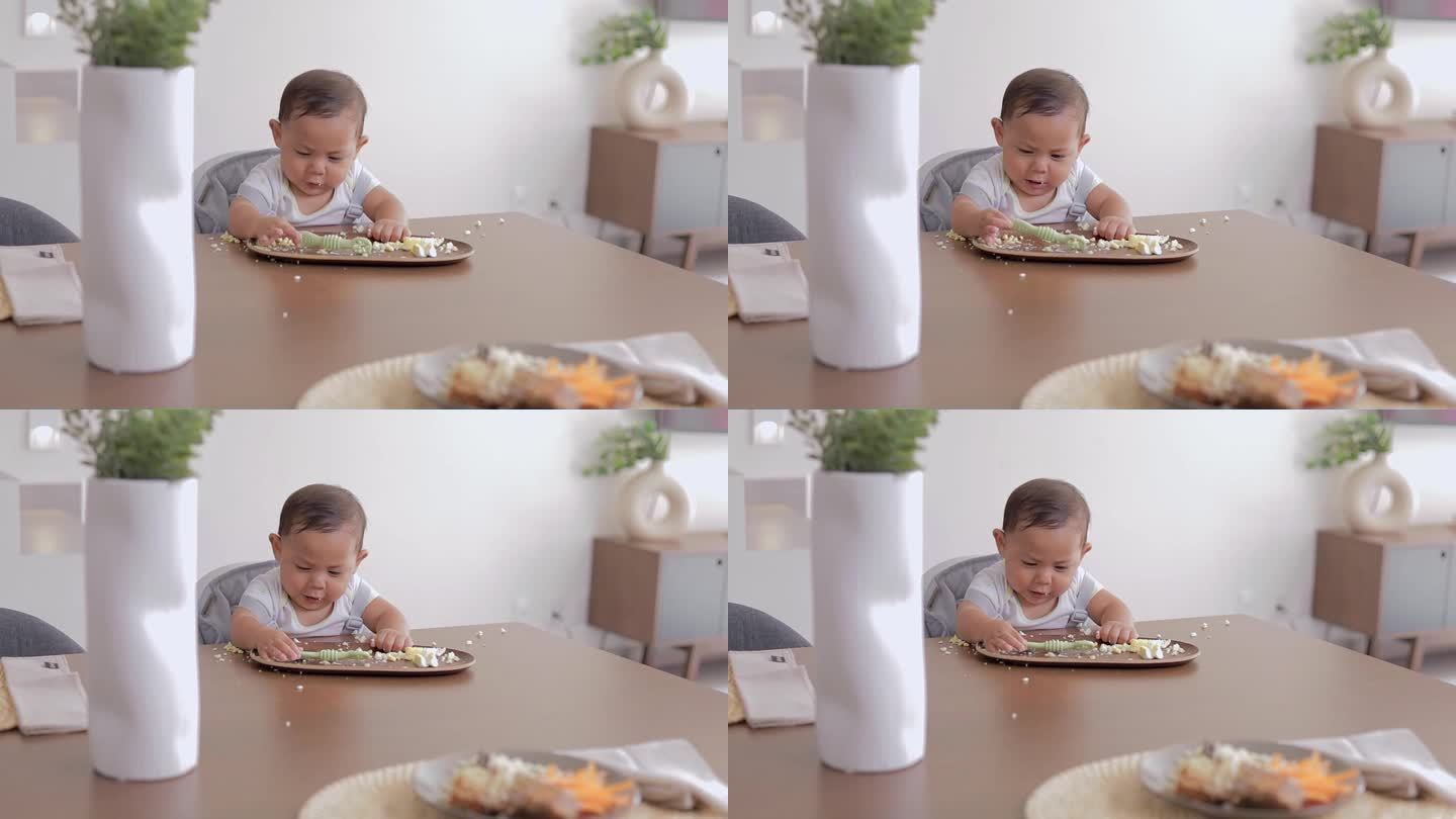 婴儿主导的断奶概念。宝宝用手坐在桌子旁吃东西，手里拿着一个预先装好的勺子
