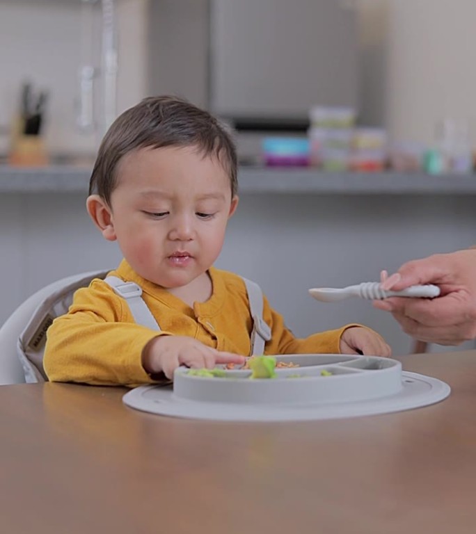 一个婴儿坐在桌边被用勺子喂的特写。婴儿主导的断奶概念。补充喂养