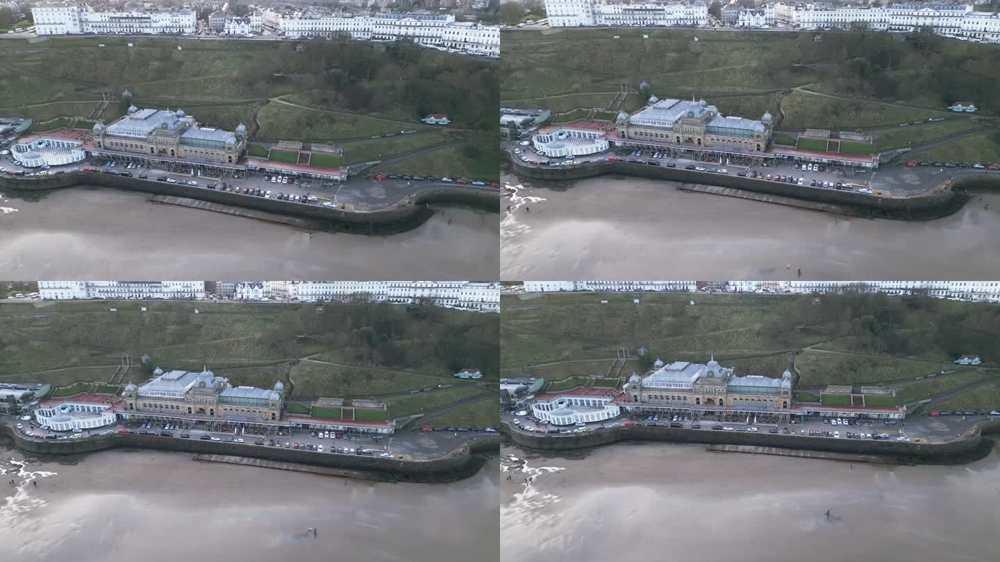 广角无人机拍摄的斯卡伯勒水疗中心位于空旷的海滩旁，白天海浪涌向海岸线，英国。
