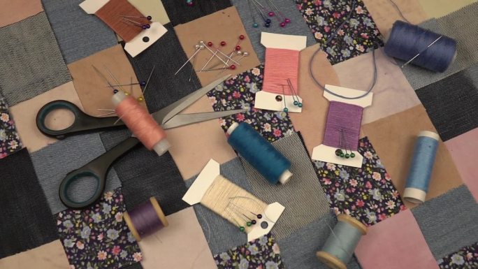 拼接缝纫的配件放在拼接纺织品上，印花棉布和牛仔布元素在蓝色色调，慢动作