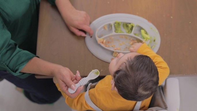 俯视图，一个孩子正在家里的桌子上用手吃东西。婴儿辅食