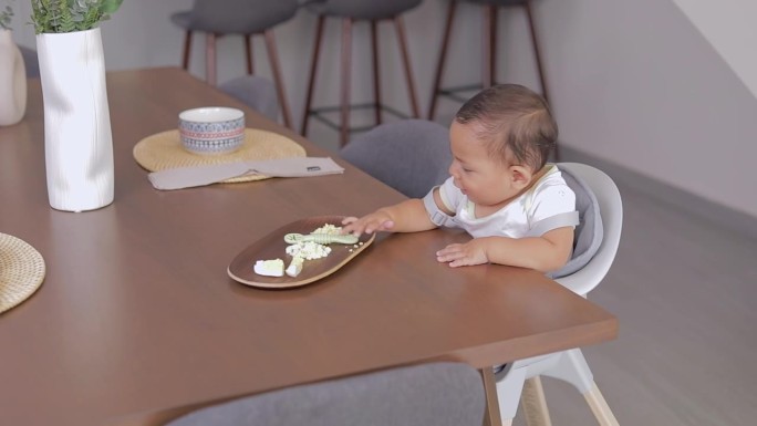 坐在桌子旁的婴儿拉起他的盘子里的食物，抓起预加载的勺子开始吃。BLW概念