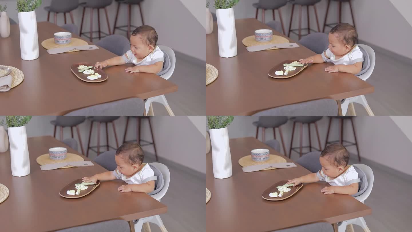 坐在桌子旁的婴儿拉起他的盘子里的食物，抓起预加载的勺子开始吃。BLW概念