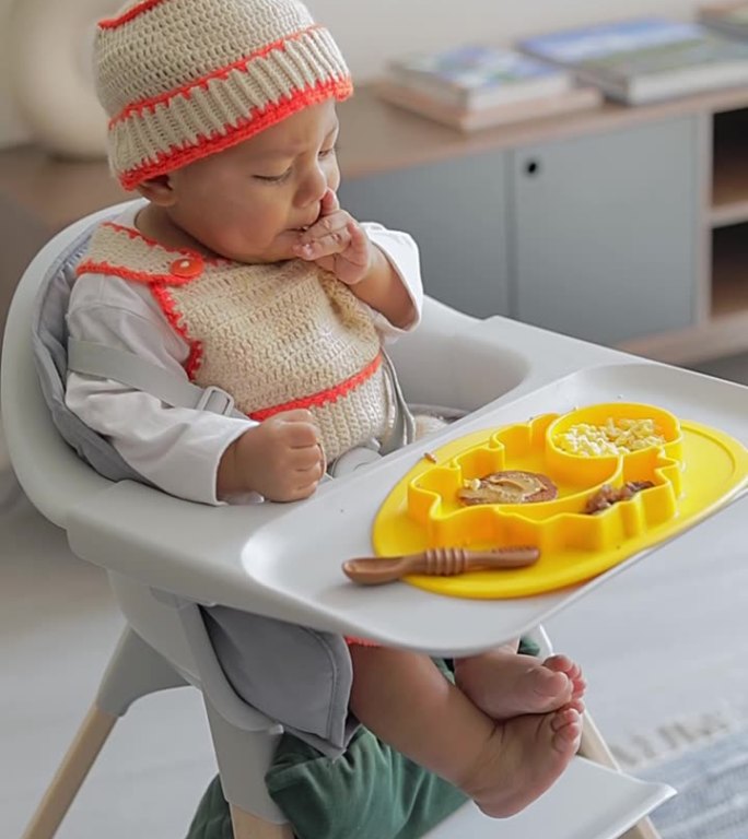 一个拉丁裔婴儿的补充喂养他坐在椅子上用蓝色的盘子吃早餐。