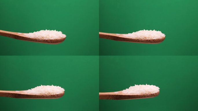 生的白色长粒米倒落在木勺旋转旋转锅绿色背景