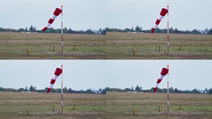 红白相间的风袜在灯光下飘扬，显示机场的风向和风速。风向标靠近森林和泥土跑道