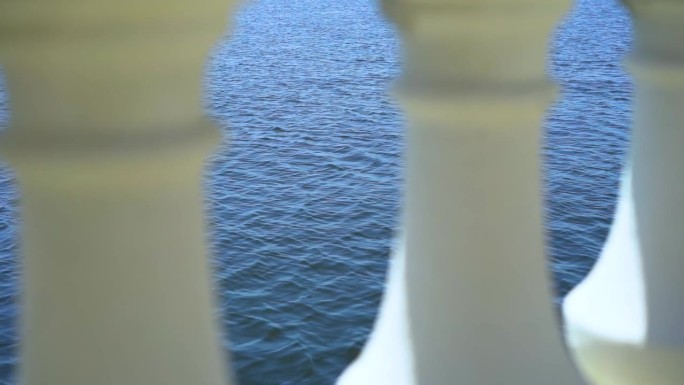 平静的蓝色海浪在装饰白色大理石阳台柱子之间移动